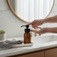 Bubble Gallery amber glass foaming soap dispenser with black pump, used in a bathroom setting.