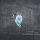 Bubble Gallery blue daisy pop-up sponge with a hanging string on a dark textured background