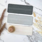 Bubble Gallery diatomaceous earth bottle tray in charcoal, light grey, and natural beige. Features subtle channels for airflow and a wooden dish brush.