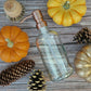 Bubble Gallery 16oz clear glass soap dispenser with a bronze metal pump surrounded by autumn pumpkins and pinecones