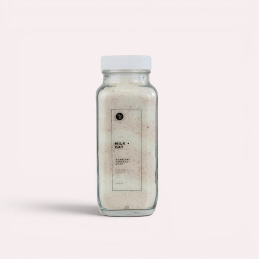 Bubble Gallery Milk + Oat Bubbling Magnesium Bath Soak in a glass jar with a white lid. Relaxing bath salts.